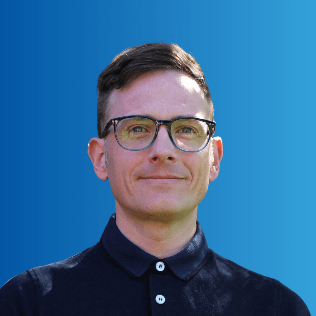 A man in glasses smiling at the camera on a blue background