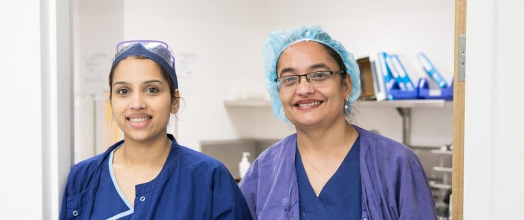 Two women in blue scrubs smiling at the camera